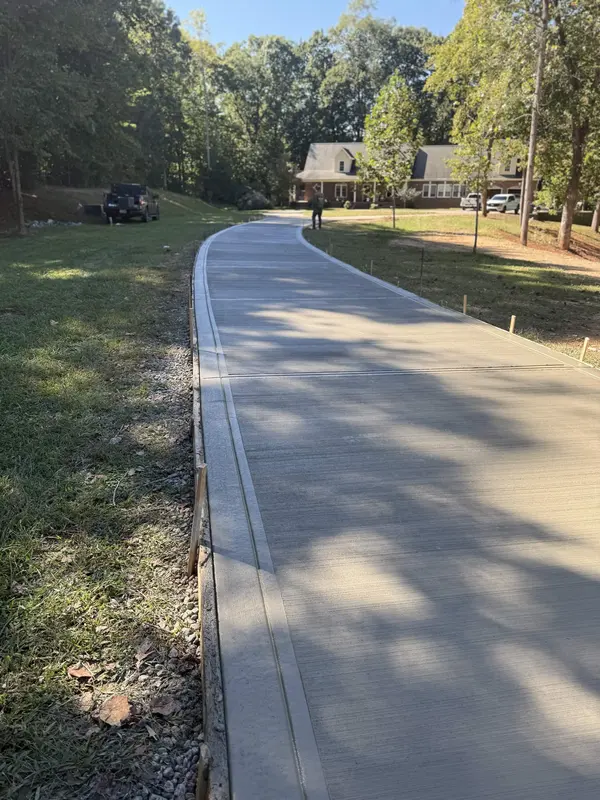 Finished broom-finish concrete driveway curving up to a brick ranch home
